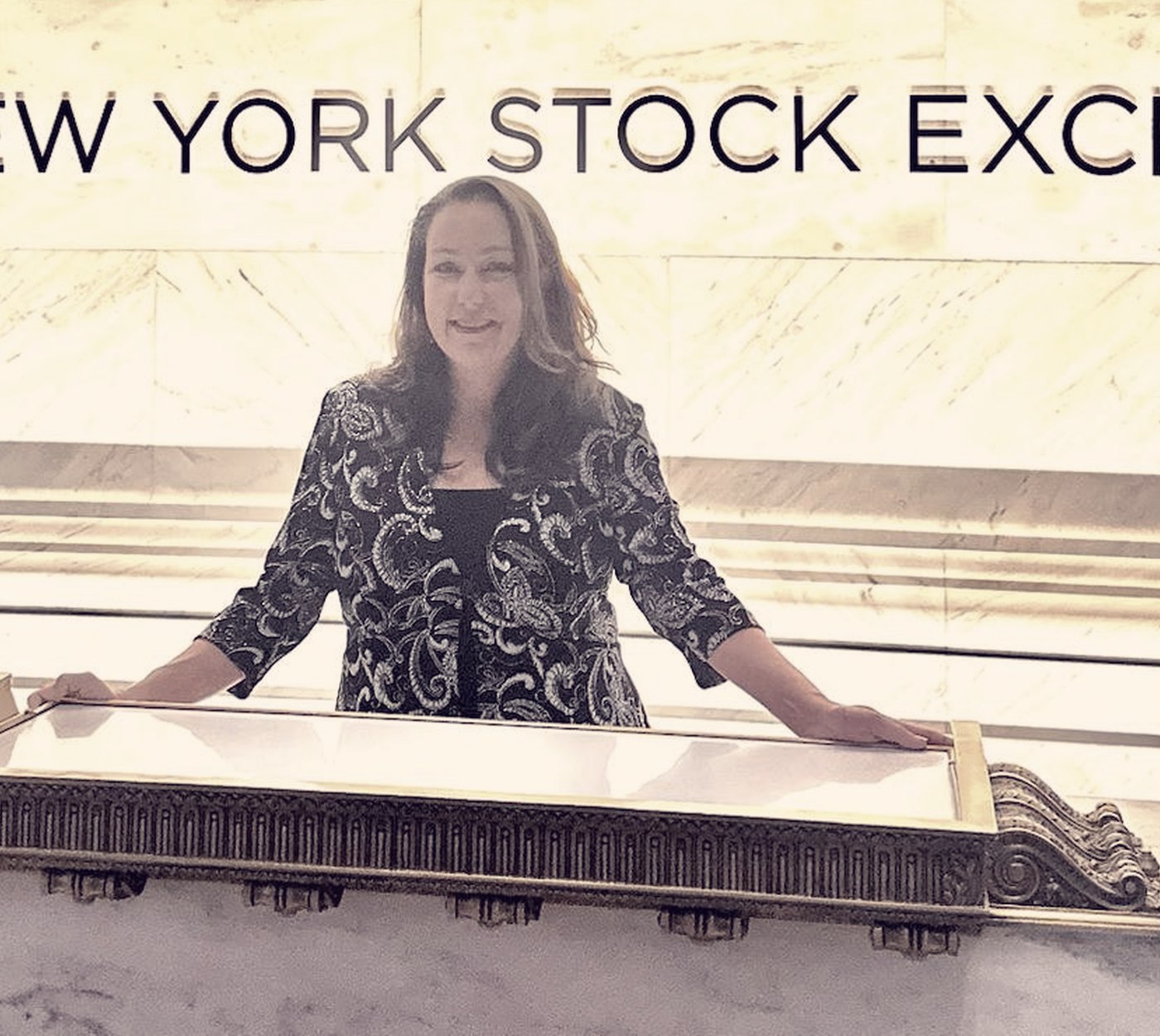 Meagan Crawford at the podium beneath the opening bell on the floor of the New York
        Stock Exchange, June 2025.